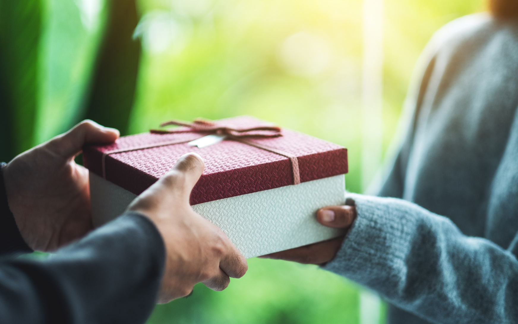 Two people exchanging a small gift wrapped with a ribbon.